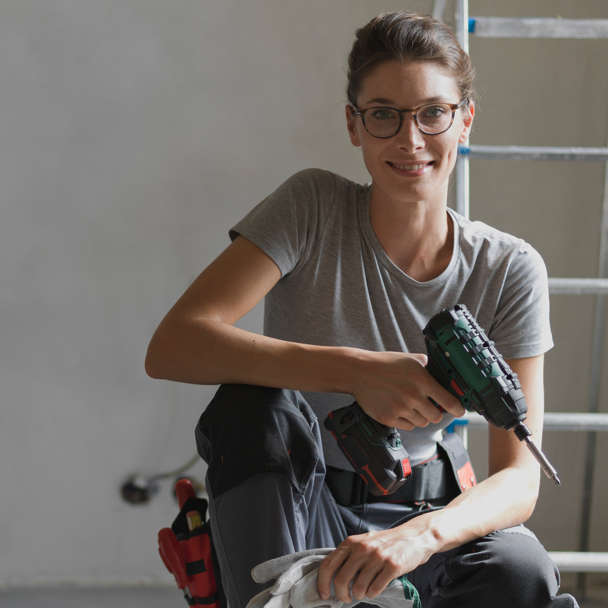 Professional repairwoman with tool belt doing a home renovation, she is posing and holding a drill