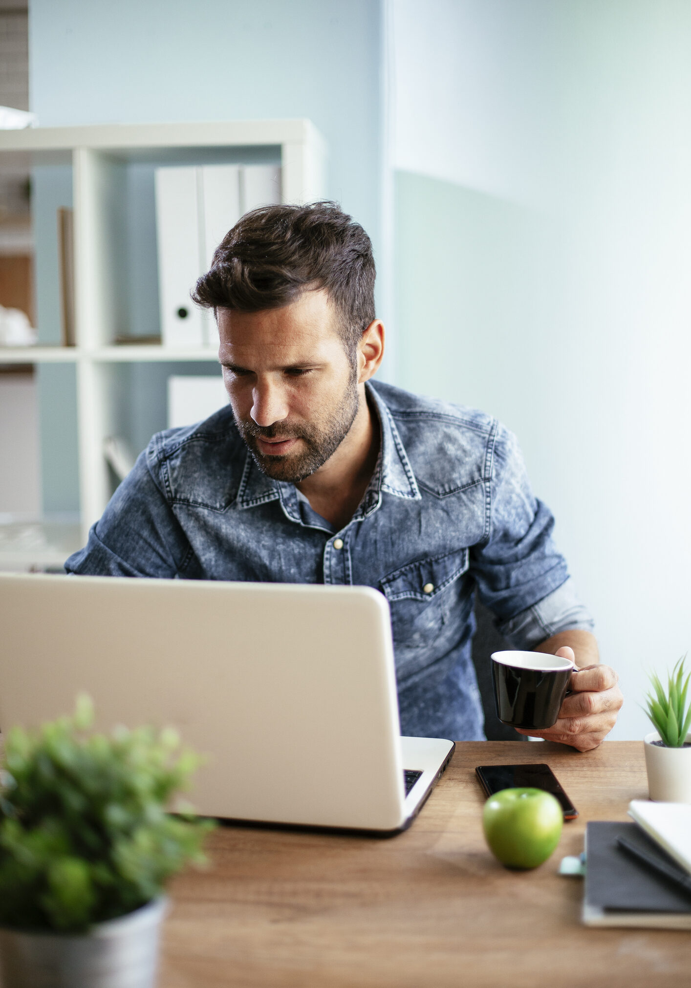Young businessman using computer and drinking coffee in his office. Handsome man on coffee break