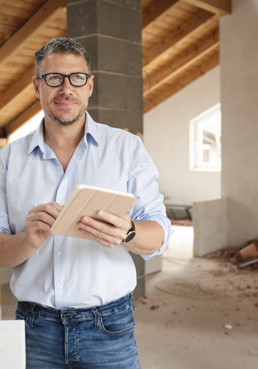 male architect middle age with black glasses stands on construction site in loft house and holds his tablet