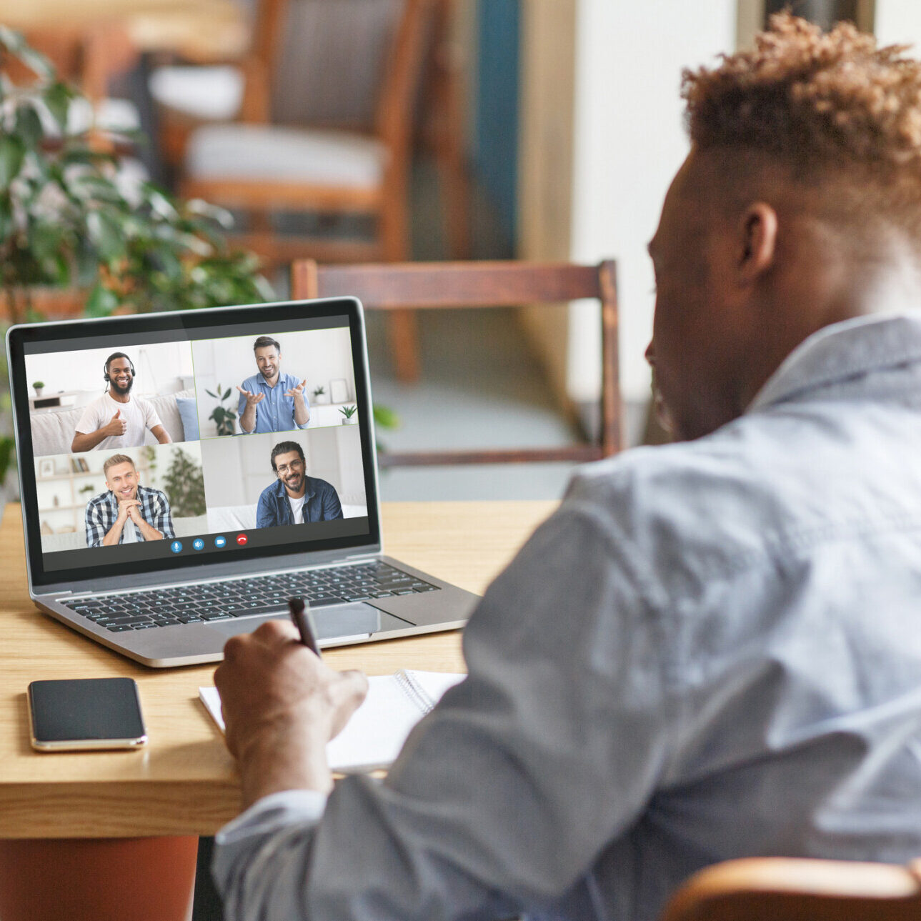 Coworking place, online communication remote, modern devices for remote meeting. Millennial african american guy sit in cafe interior and look at laptop with headshot of multiracial friends on screen